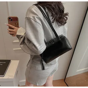 Dettaglio borsa a spalla in pelle liscia nera con doppi manici e logo del marchio