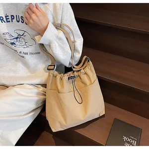 Détail d'un sac seau en nylon kaki avec cordon de serrage et poche avant sur escalier en bois