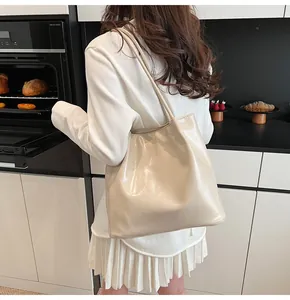 Detailed side view of large glossy cream leather tote bag worn by a model on shoulder