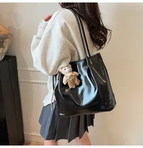 Detail of glossy black leather tote bag featuring a cute plush bear pendant on the side