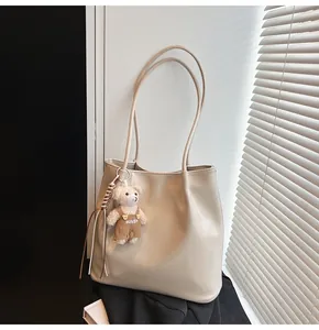 Detail of beige soft leather tote bag with a cute brown bear charm and slim straps