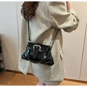Détail du sac bandoulière en cuir verni noir avec boucle cœur argentée sur modèle