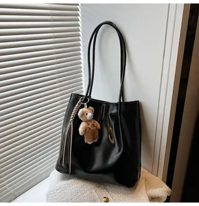 Detail of glossy black leather tote bag with cute brown bear charm and long shoulder strap
