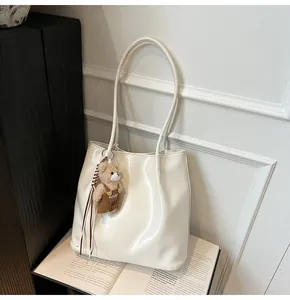 Detail of off-white glossy leather tote bag featuring a cute plush bear charm accessory