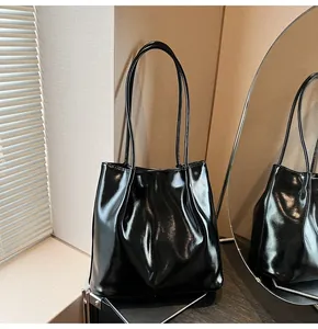 Detail of a black glossy leather tote bag with elegant shoulder straps in a modern setting