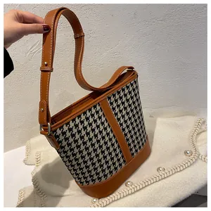 Detailed close-up of houndstooth canvas bucket bag with brown leather accents and strap