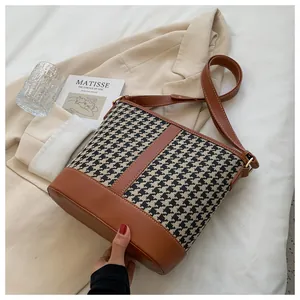 Detail of houndstooth bucket bag with brown leather trim and golden metal buckles