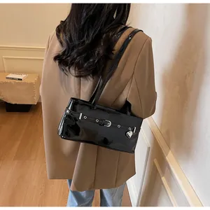 Détail d'un sac sous le bras en cuir verni noir avec boucle argentée et pendentif cœur