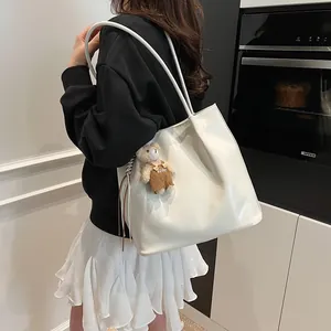 Minimalist white leather tote bag with cute brown bear charm worn on shoulder