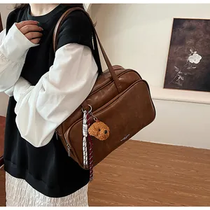 Close-up of brown PU leather Boston bag with teddy charm and luxury logo detail