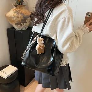 Chic black glossy leather tote bag with a cute bear pendant on a shoulder strap