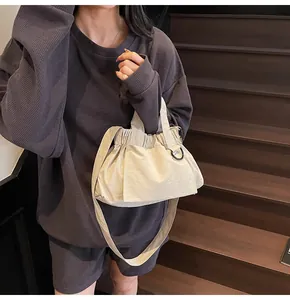 Detail of beige pleated fabric crossbody cloud bag worn by model on wooden stairs