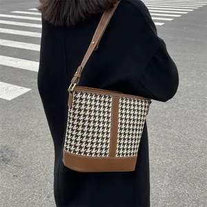 Fashionable houndstooth bucket bag with leather trim worn as a stylish crossbody bag