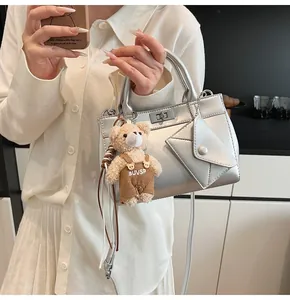 Detailed view of silver matte handbag with metal turn-lock and cute bear plush charm