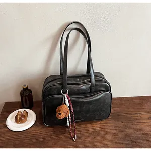 Detail of grey Boston bag with plush dog charm and braided cord on a wooden desk