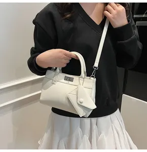 White minimalist crossbody bag with top handle and small envelope charm worn by model