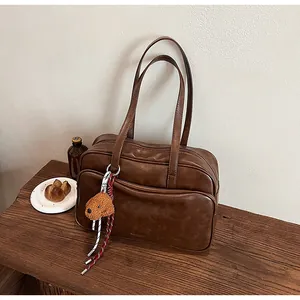 Detailed view of brown PU leather Boston bag with a teddy bear charm on wood table