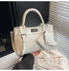 Close-up of white crossbody bag with silver twist lock and decorative mini envelope pouch
