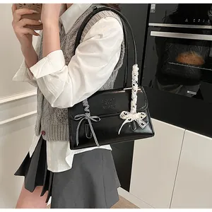 Detail of black glossy shoulder bag featuring lace bow charms and embossed brand logo