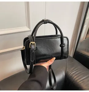 Détail d'un sac à main en cuir verni noir avec lettres embossées et boucles dorées