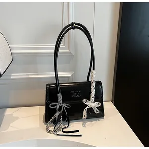 Detail of black glossy leather handbag featuring elegant ribbon bows and silver bead chain