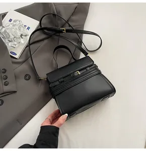 Détail du sac bandoulière noir avec boucle dorée sur un blazer gris, accessoire de mode