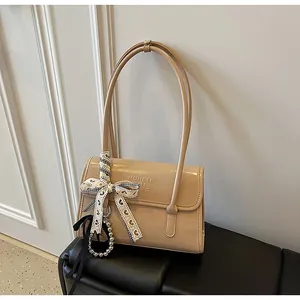 Detail of beige glossy shoulder bag with heart ribbon and beaded charm on leather