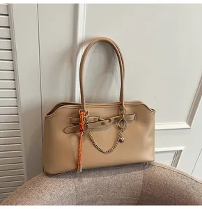 Detail of beige tote bag featuring orange woven cord and golden heart charm chain