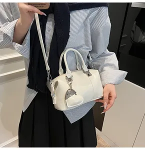 Detail of white Boston bag with leather heart charm and adjustable shoulder strap