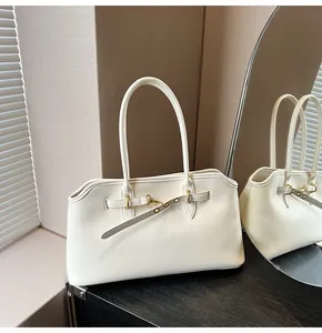 Detail of ivory leather shoulder bag showing wavy top edge and gold buckle on black wood