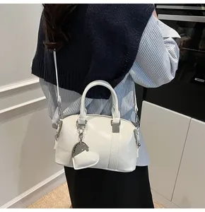 Detail of white Boston handbag with heart charm and textured PU leather on a model