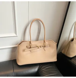 Detail view of a beige leather tote bag with gold eyelet strap on a black sofa