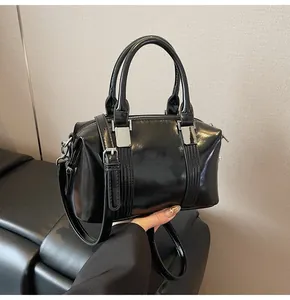 Close-up of a black Boston bag with glossy mirror finish and silver metal hardware details