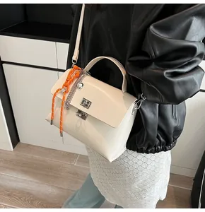 Detailed close-up of cream leather handbag featuring metal twist lock and heart chain charm