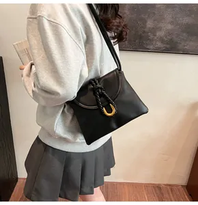 Detail of black leather shoulder bag with woven knot and gold U-shaped metal ring on model