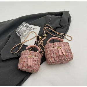 Détail de sacs seaux en tweed rose avec chaînes dorées sur fond de tissu gris