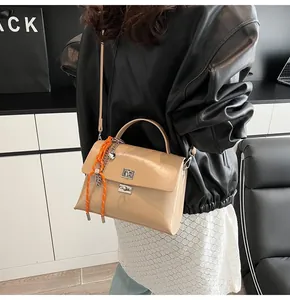 Detail view of the beige faux leather crossbody bag with silver twist lock and woven charm