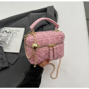 Détail du mini sac à main en tweed rose avec double zip doré et bandoulière sur tissu gris