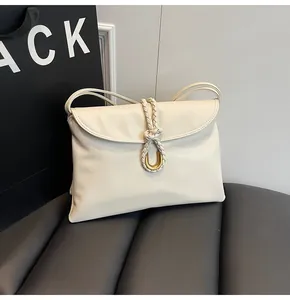 Detail of cream shoulder bag featuring woven knot buckle and gold U-shaped hardware