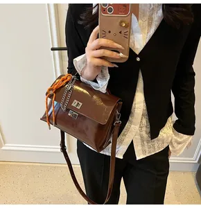 Detail of dark brown glossy crossbody bag with orange rope handle and metal lock