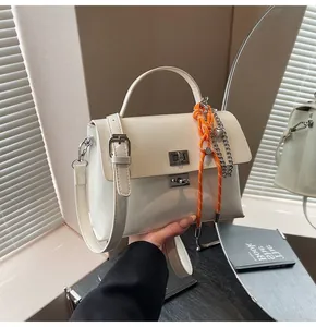 Detail of cream white handbag with silver twist lock and orange braided charm