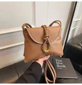 Detail of caramel brown crossbody bag featuring woven strap and golden U-shaped hardware