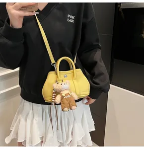 Detalle de mini bolso amarillo de piel con colgante de osito de peluche y bandolera fina