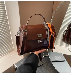 Detail of dark brown leather messenger bag with silver twist lock and woven charm accent