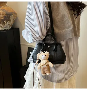 Detalle de bolso bandolera de cuero granulado negro con colgante de osito de peluche
