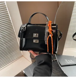 Detail of black faux leather handbag featuring dual turn-lock closure and orange cord charm
