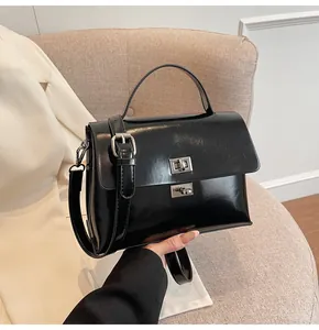 Detail of black glossy leather handbag with silver metallic buckle on a beige sofa