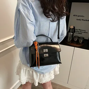 Minimalist black patent leather messenger bag with orange charm and silver square lock