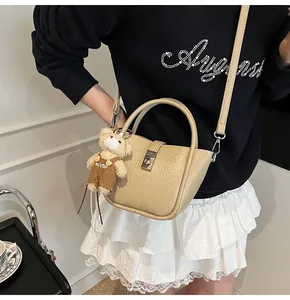 Détail du sac seau beige à motif litchi avec un pendentif d'ours en peluche mignon