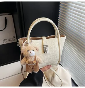 Détail du sac seau en cuir crème avec fermoir argenté et charmant pendentif d'ours en peluche